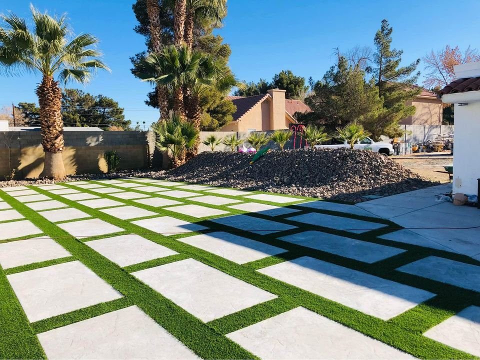 a backyard pool area with concrete squares with artificial grass strips in between